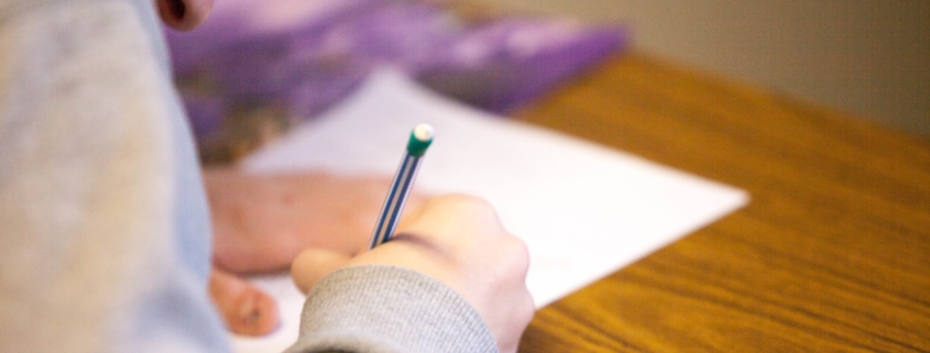 student writing on paper hunched over desk