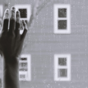 depression hand against window with rain, house in the background