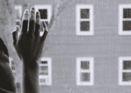 depression hand against window with rain, house in the background