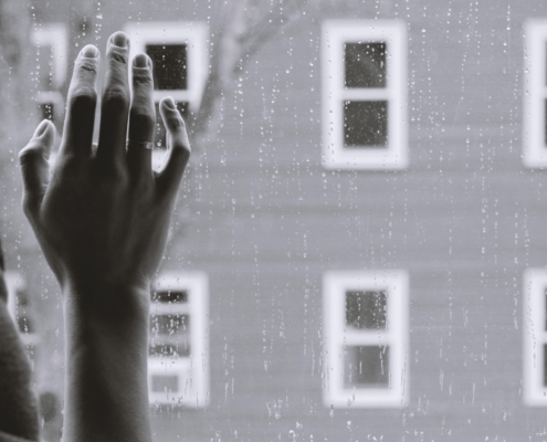 hand against window with rain, house in the background