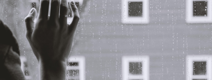 depression hand against window with rain, house in the background