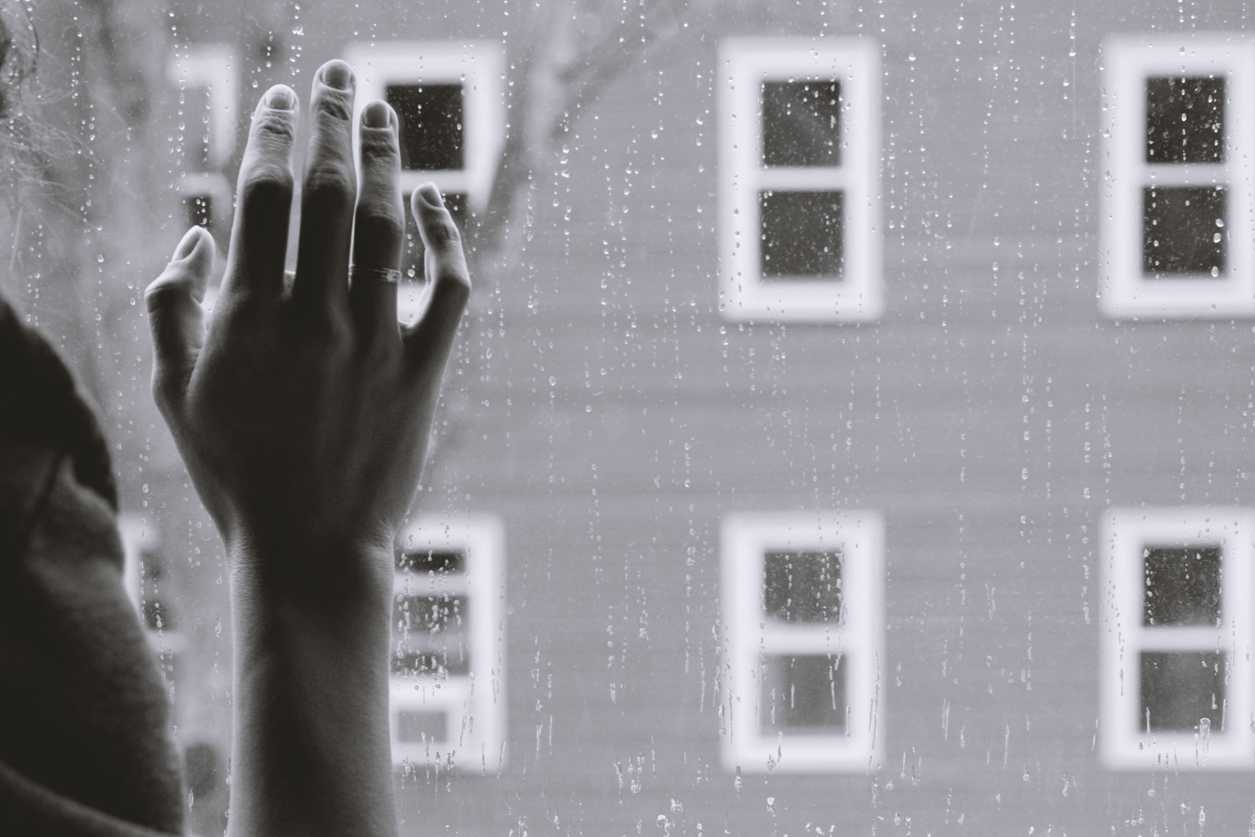 depression hand against window with rain, house in the background