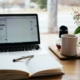 open notebook and coffee mug in front of laptop open for studying